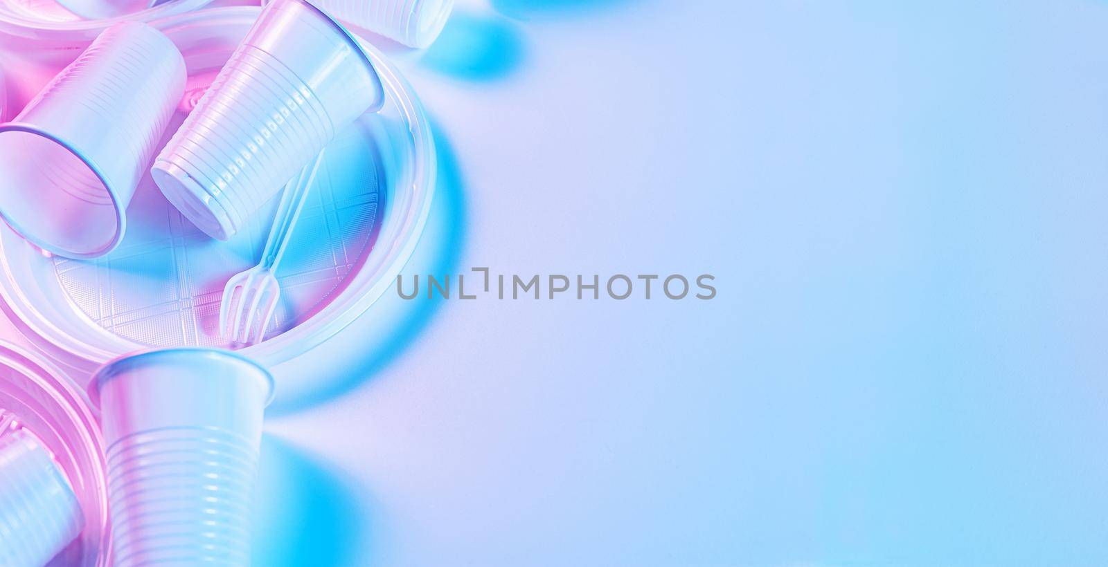 Various disposable plastic tableware, cutlery on a light background in pastel colors. Minimalistic ecologically clean still life. Pop Art. And ecology problem concept. Copy space.