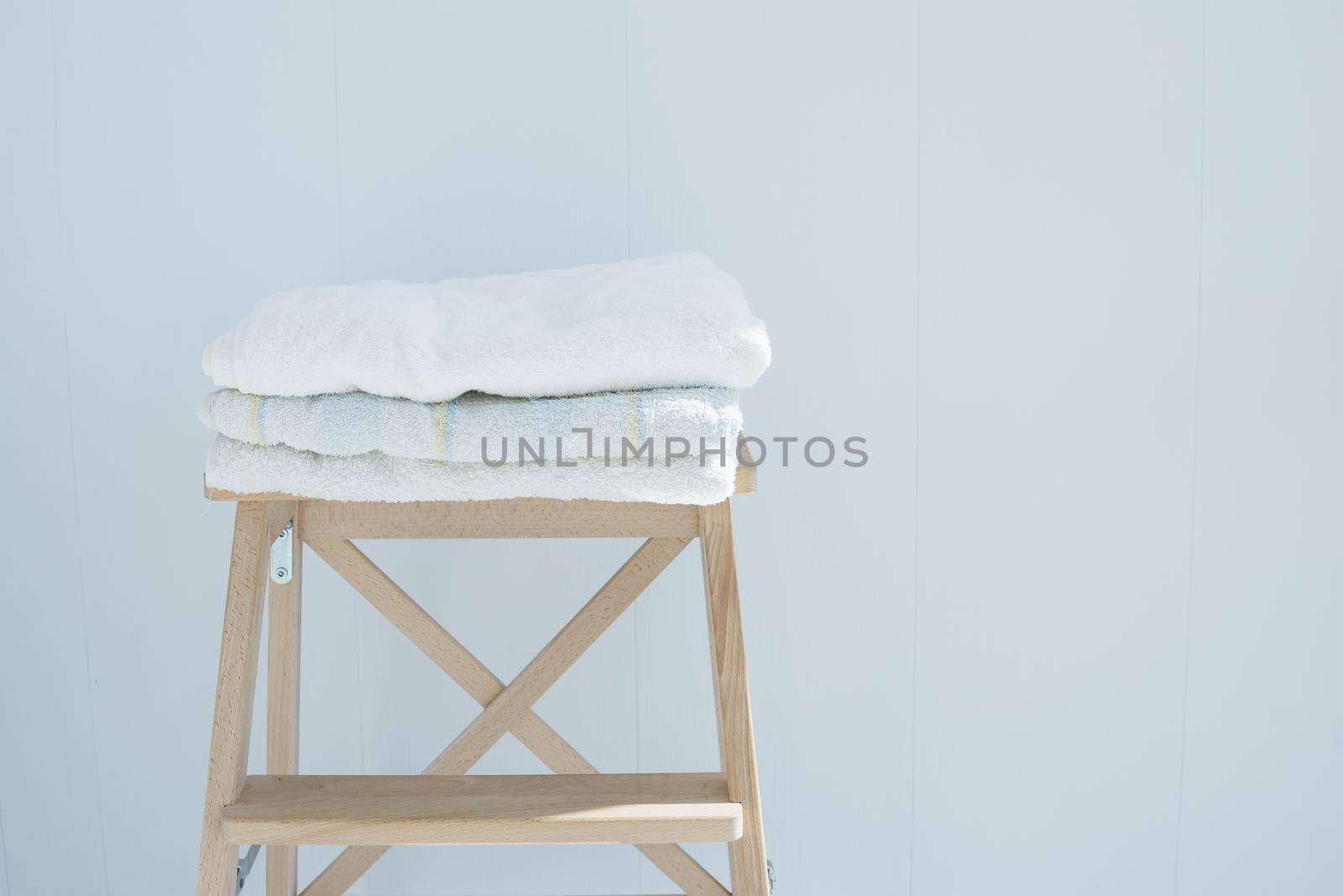 stack of clean bath towels colorful cotton Terry textile stacked on wooden chair near white wall pile concept closeup country style