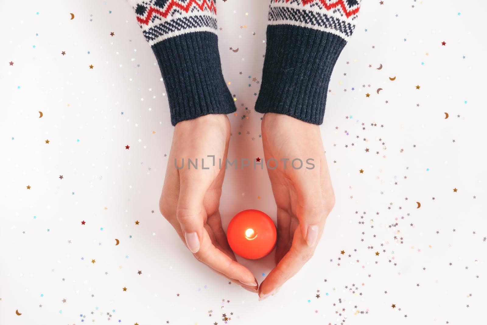 Female hands in sweater with red burning candle. Winter holiday, Christmas or Valentine's day background. Giving warmth and love concept. Xmas backdrop for design projects, postcards. New Year theme