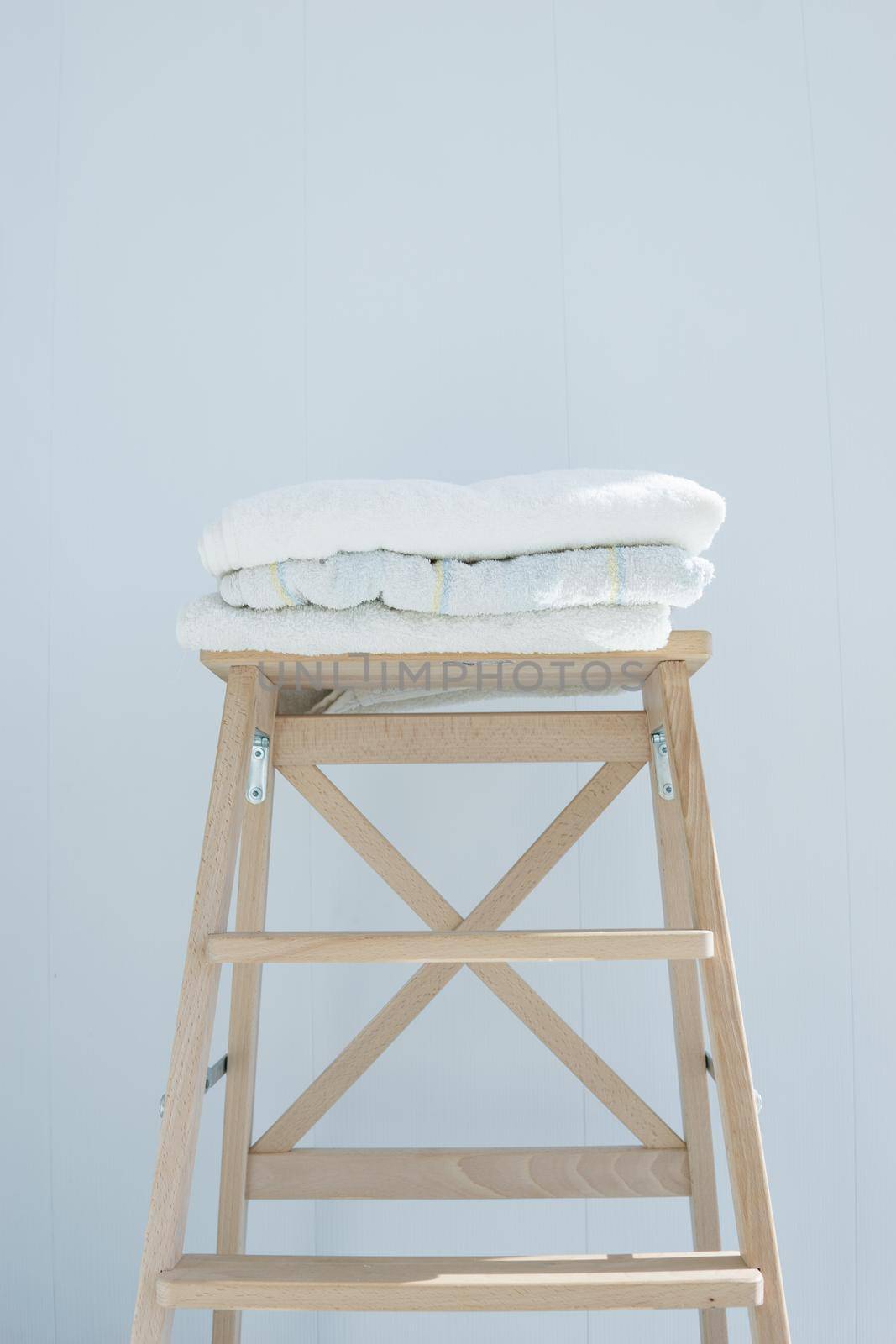 stack of clean bath towels colorful cotton Terry textile stacked on wooden chair near white wall pile concept closeup country style