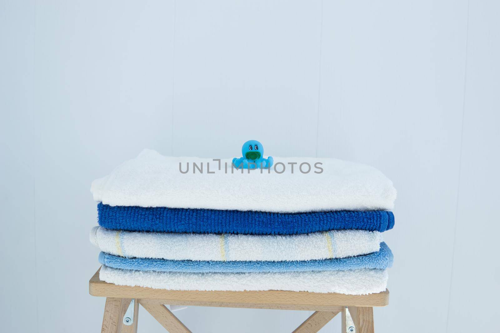 A stack of clean bath towels colorful cotton Terry textiles stacked on a wooden chair against a white wall NAP concept close up country style. Children's rubber bath toys.