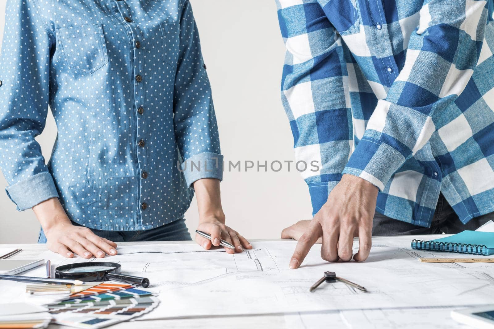 Man and woman together working at design project. Creative teamwork at workspace with construction blueprint and color swatches. People standing near desk and discussing in architecture studio.