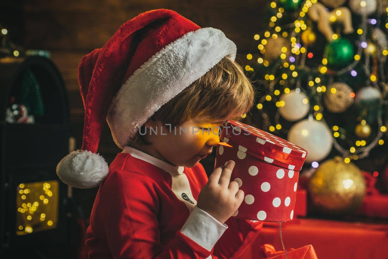 Surprised boy child open christmas gift near christmas tree. Lovely baby enjoy christmas. Funny kids face closeup. by Tverdokhlib