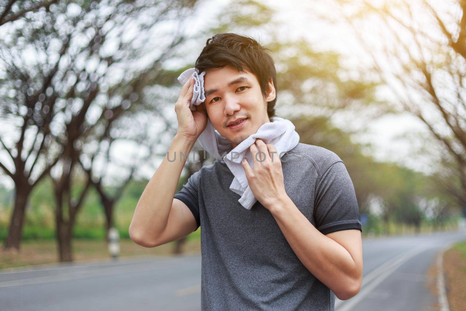 young sporty man resting and wiping his sweat with a towel after workout sport exercises outdoors at the park