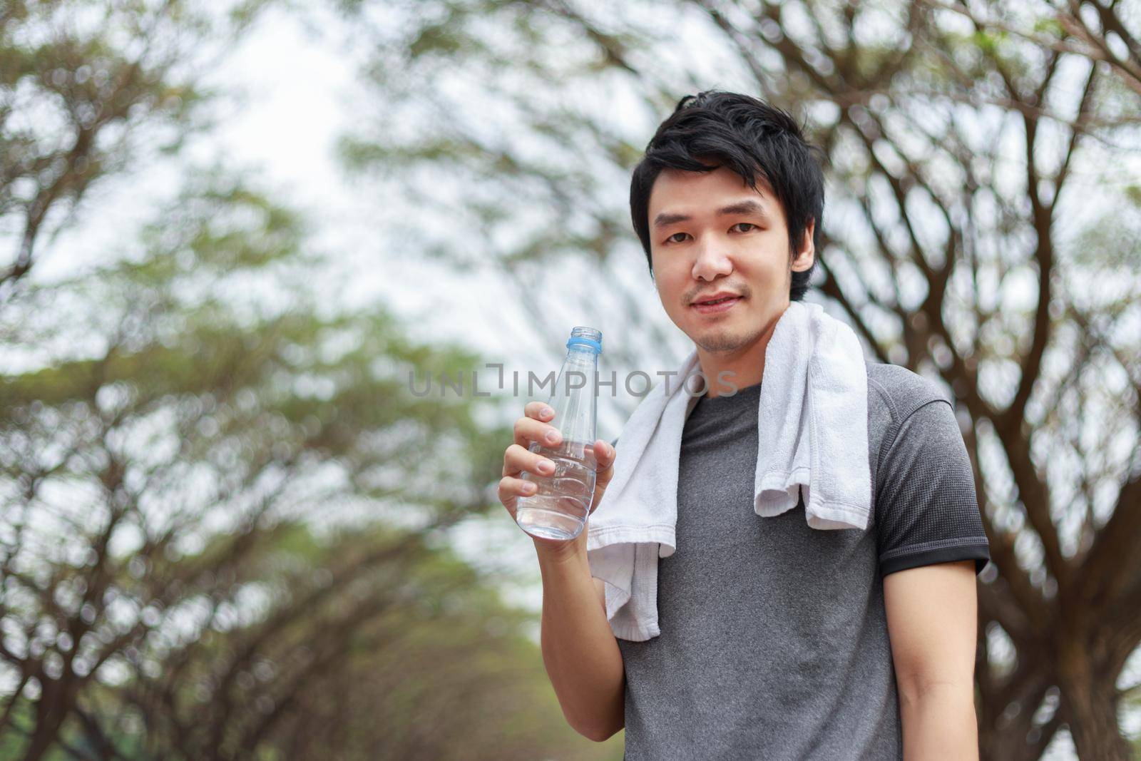 young sporty man with bottle of water in park by geargodz