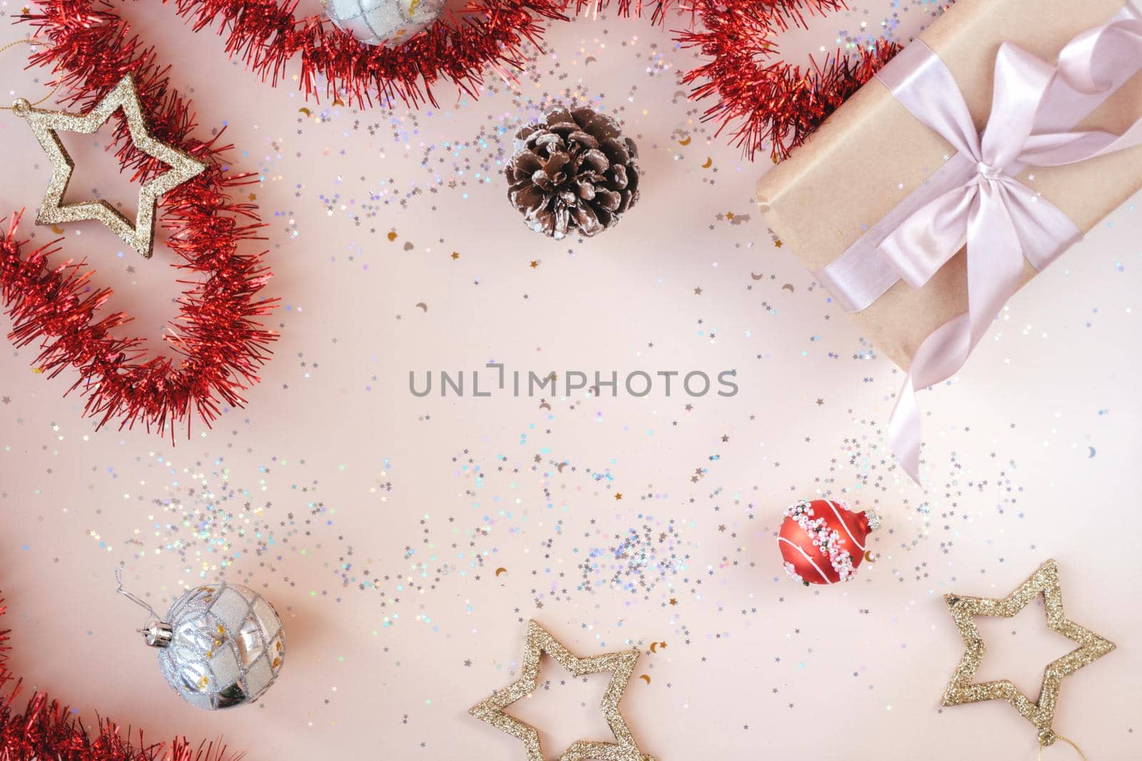 Christmas or New Year festive background with space for text. Present in kraft paper with pink ribbon on soft beige background with glitter, stars, balls, confetti, tinsel. Xmas composition. Flat lay