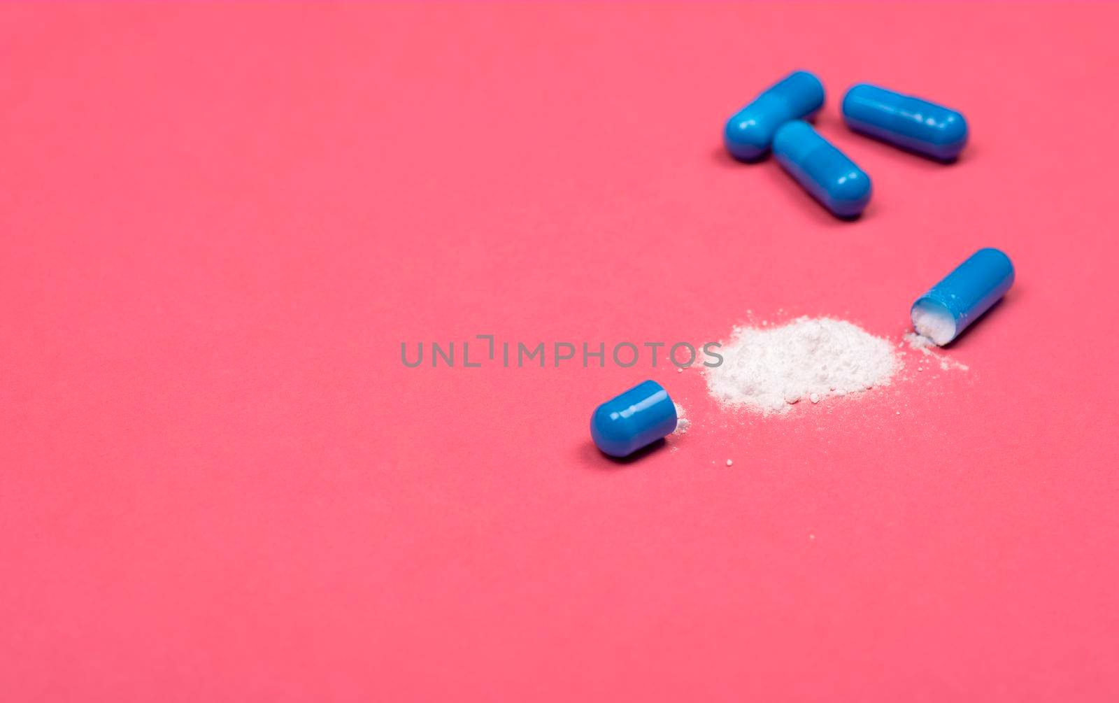 Medical background. Open blue capsule pill on pink background. Blue capsules pill spread on fuchsia background with copy space.