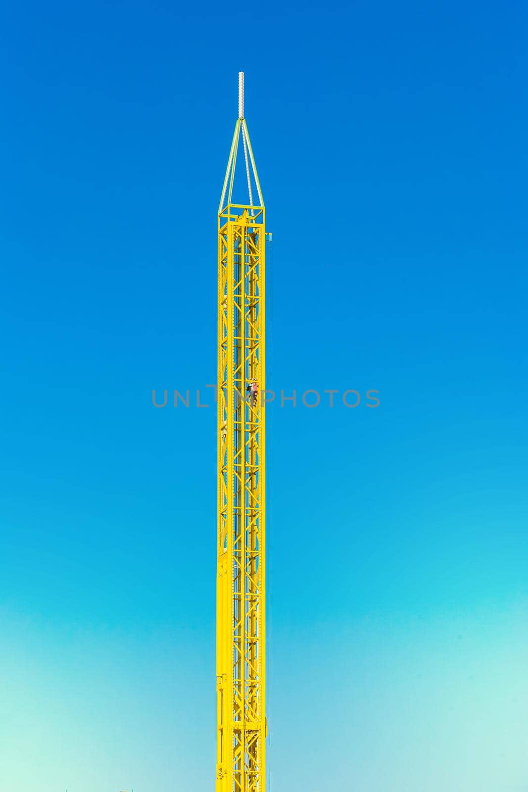 Attraction yellow tower in an amusement park against a blue sky background.