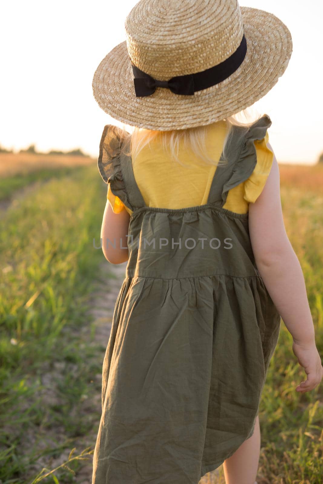 A little blonde girl in a straw hat walks in a field with a bouquet of daisies. The concept of walking in nature, freedom and an eco-friendly lifestyle.