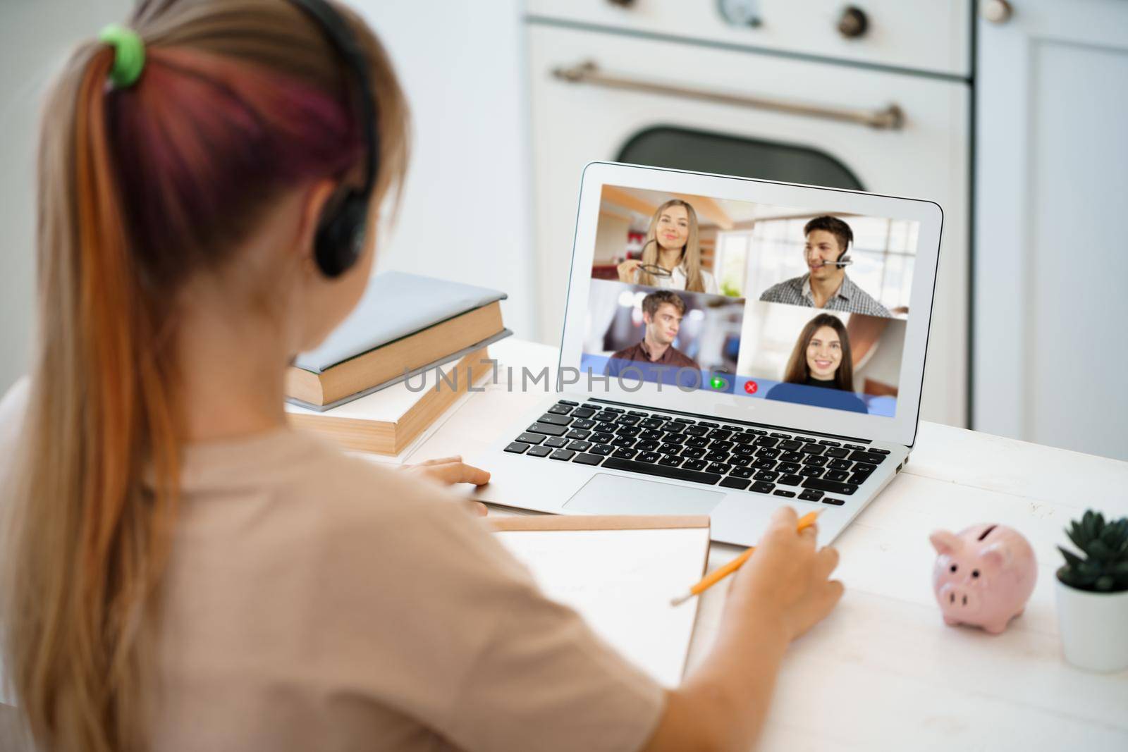 A girl is communicating via video call with classmates on laptop at home, online education