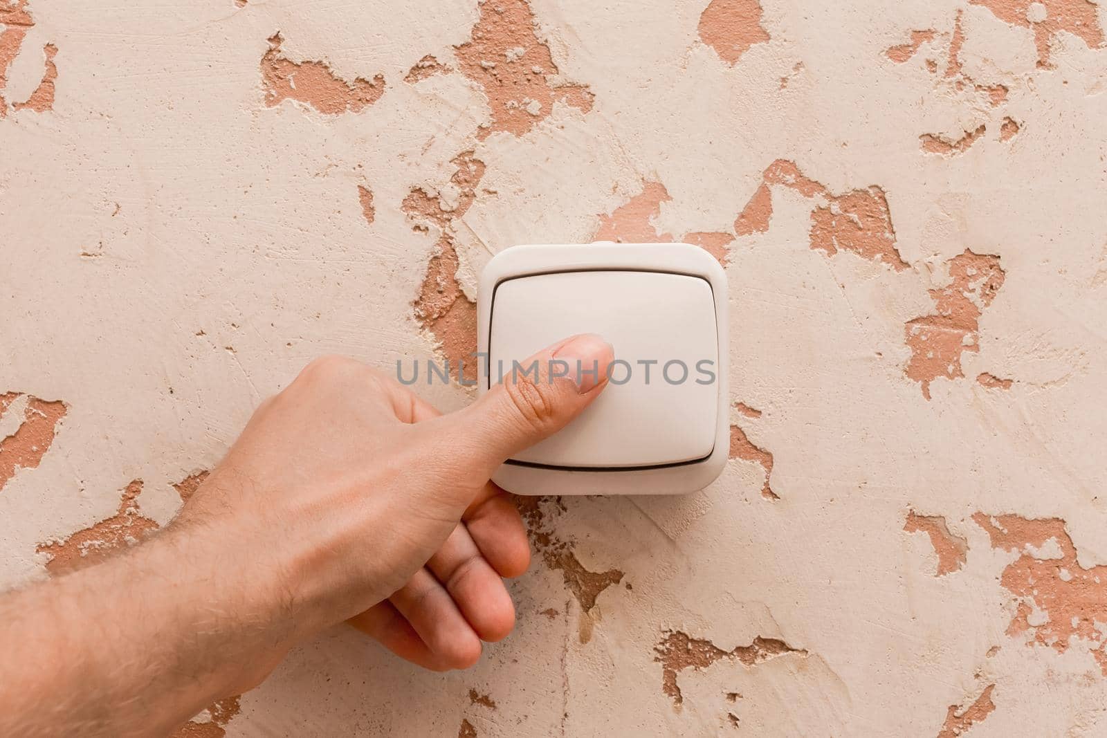 The man's hand turns off the light with an electric switch in a modern room interior background.