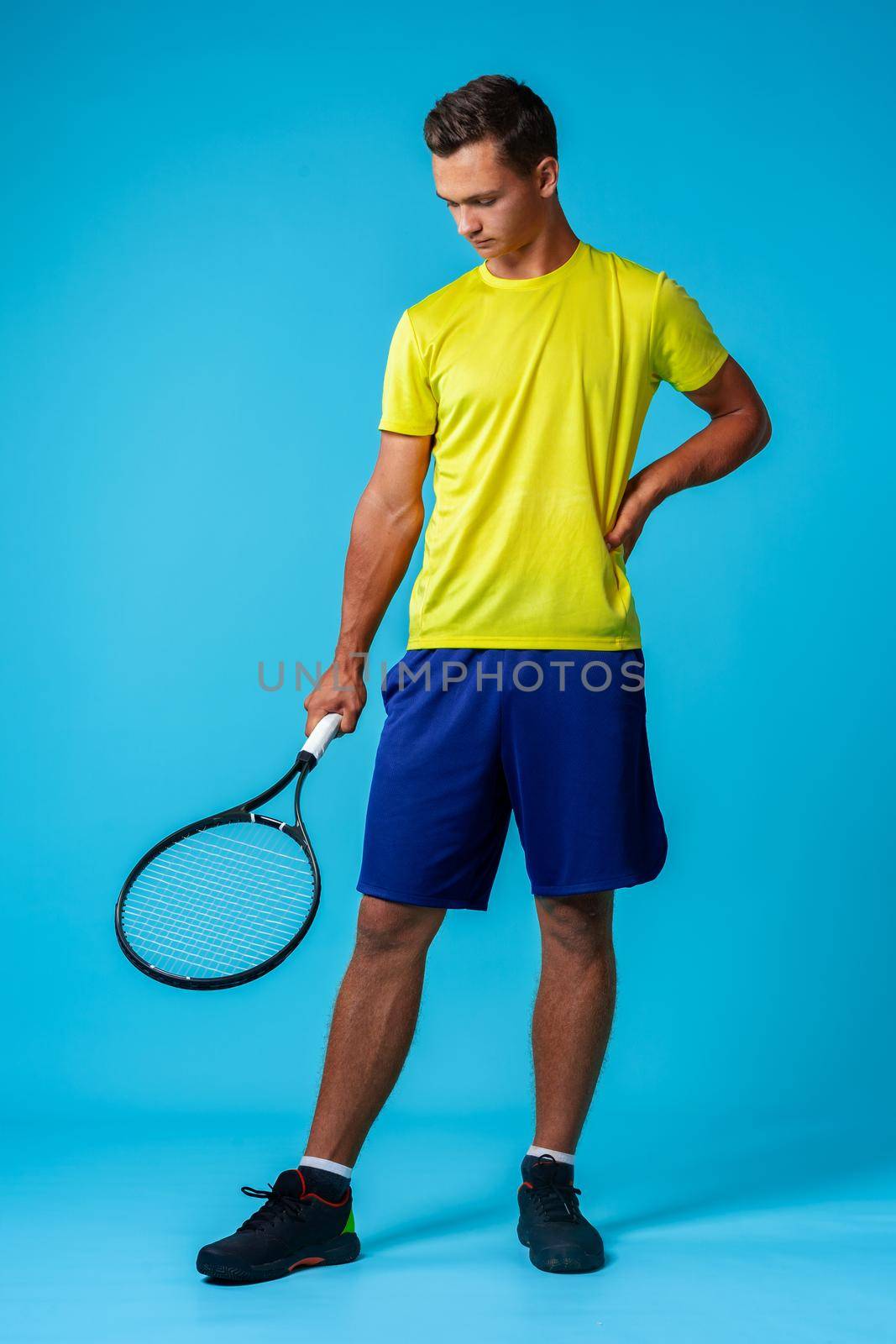 Full length studio portrait of a tennis player man on blue background close up