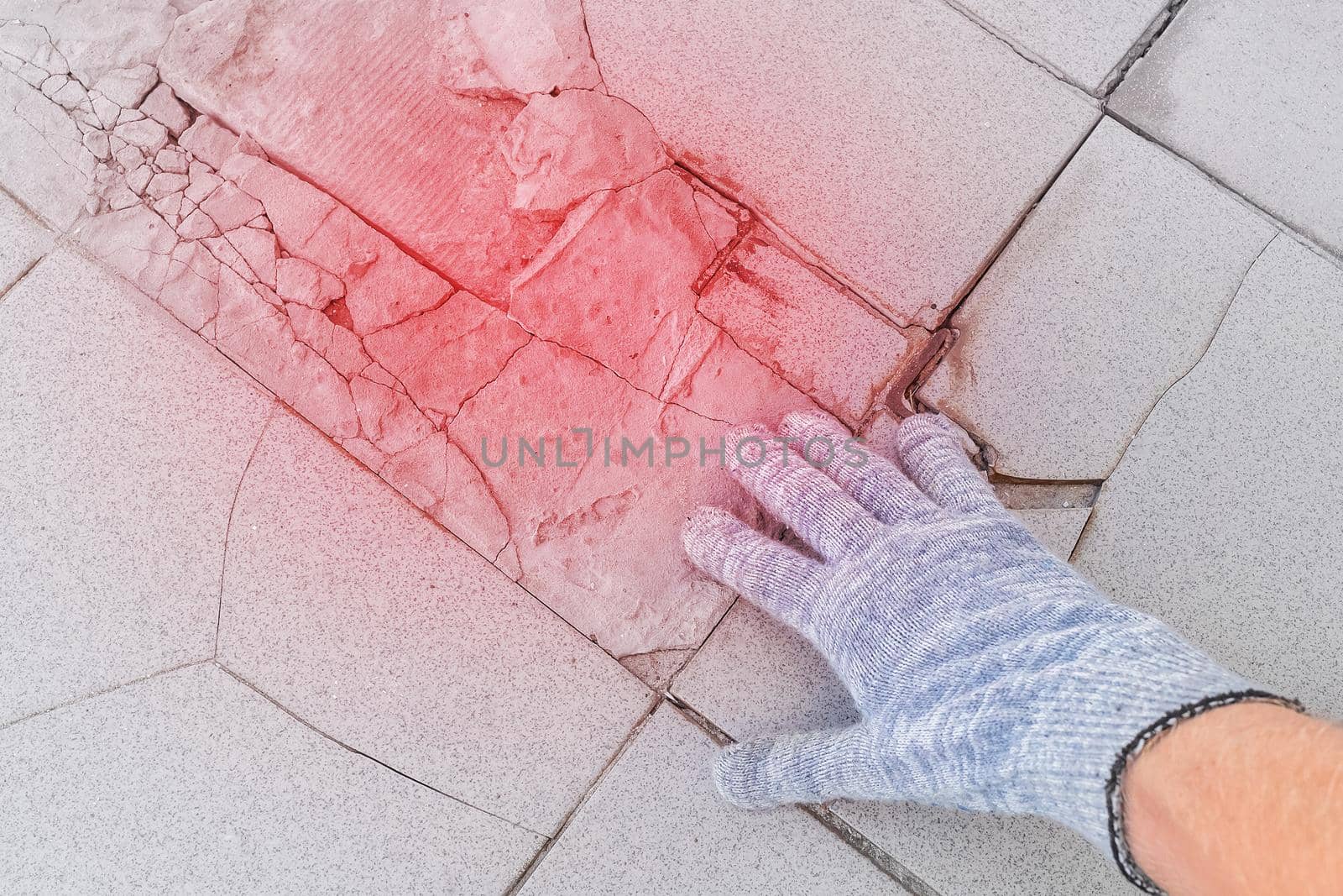 Hand of male construction worker in protective gloves examines old broken tile floor background. Renovation concept.