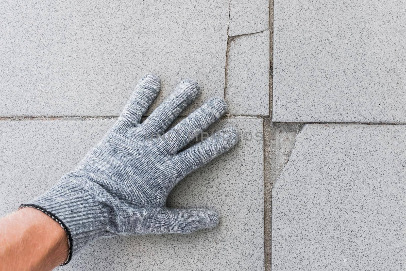 Hand of construction worker in protective gloves examines old broken tile floor background. Renovation concept.