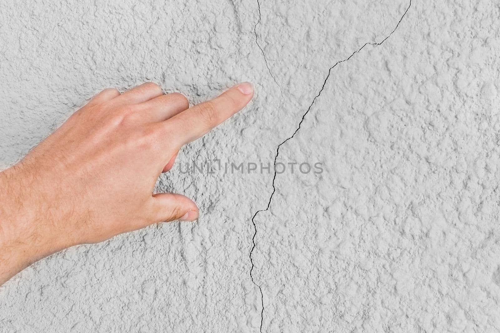 Male construction worker hand points cracks on white wall background. Renovation concept.