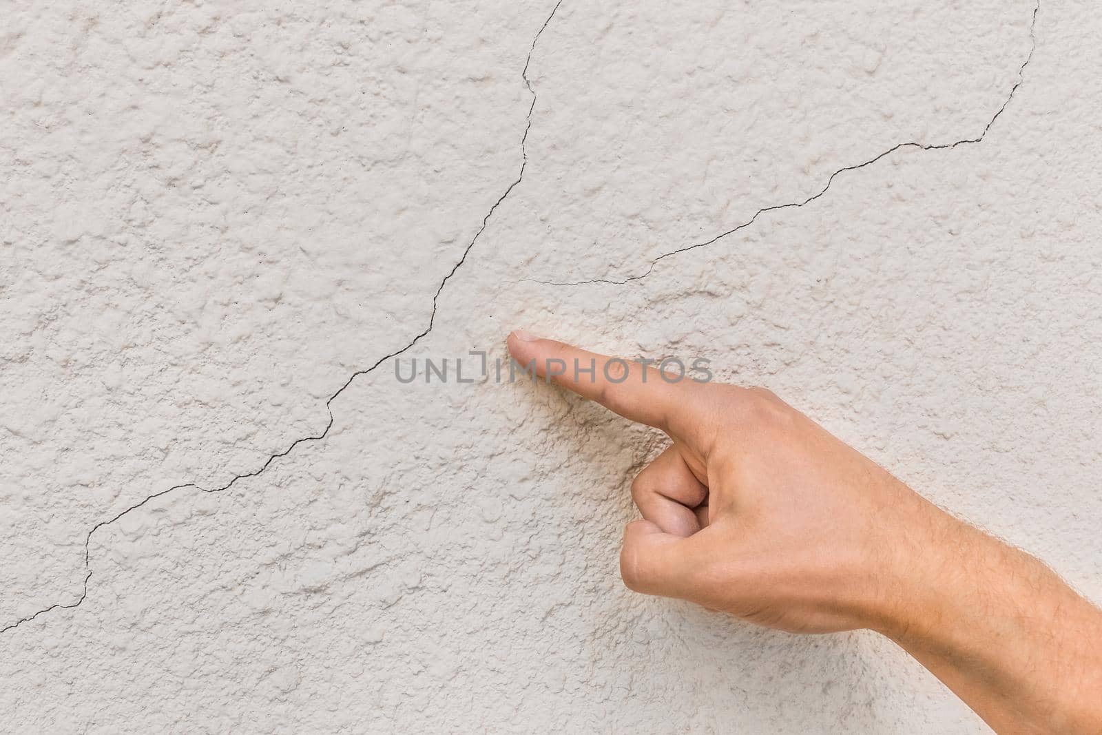 Male construction worker hand points cracks on white broken wall background. Renovation or repair concept.