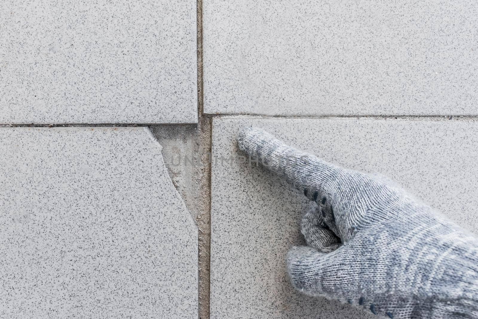 Hand of industrial worker in construction glove points on damaged gray tile background. Renovation concept.