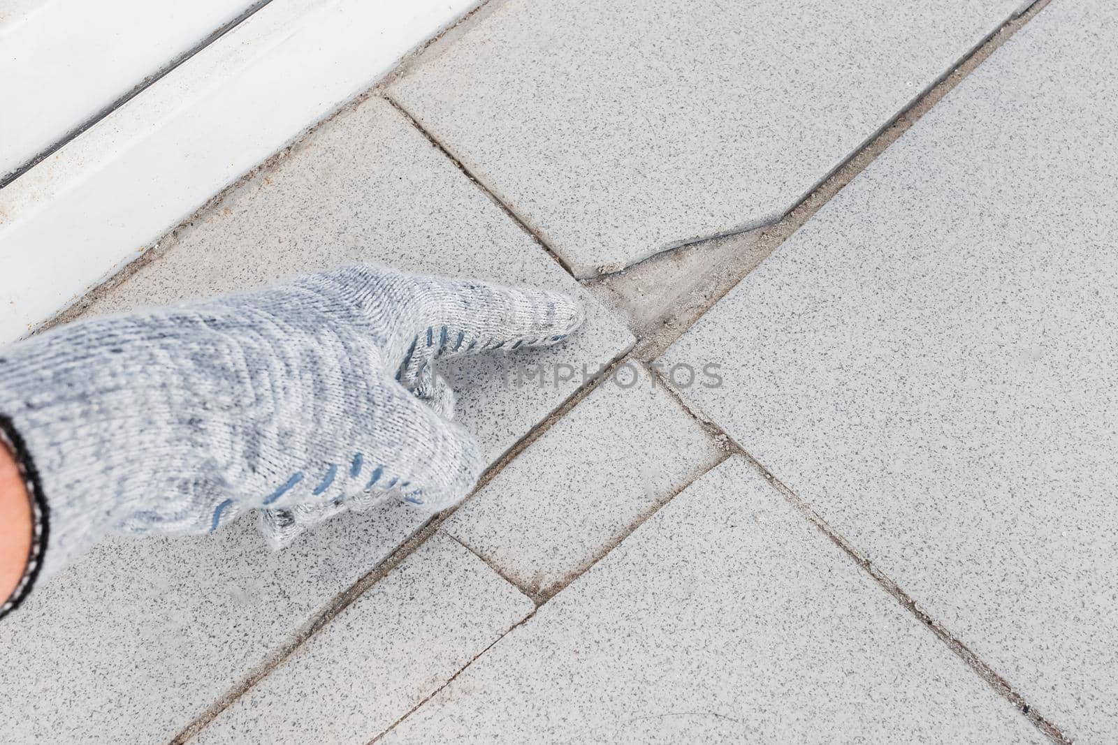 Hand of industrial worker in construction glove points on damaged gray tile background. Renovation concept.