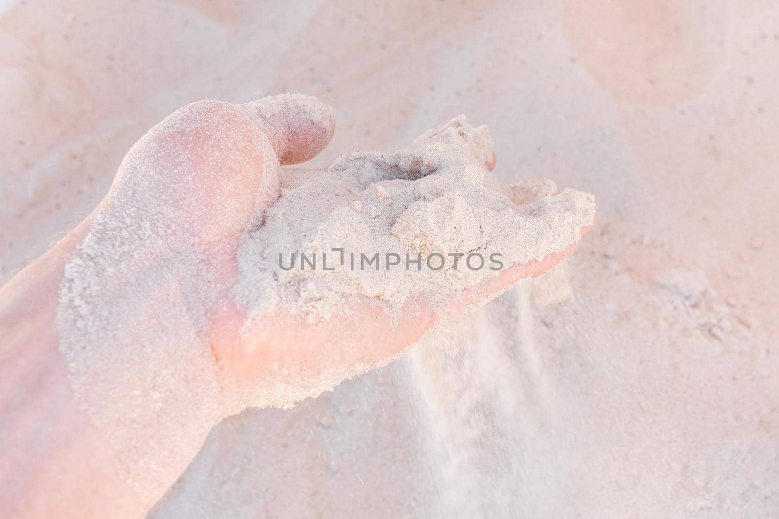 The guy's hand takes or touches the white beach sand close up.