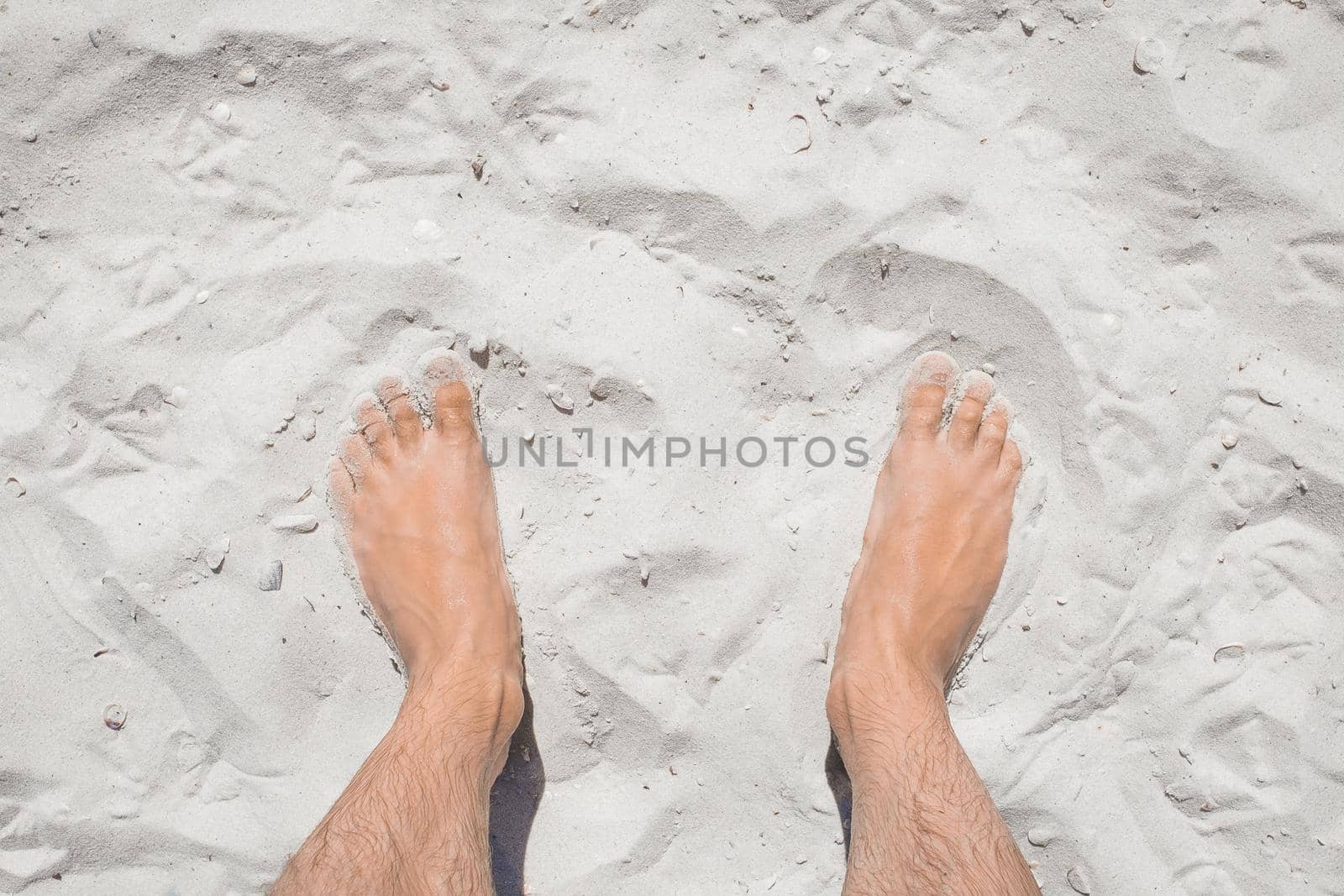 The young man's legs stand relaxed on the white beach sand, the view from above.