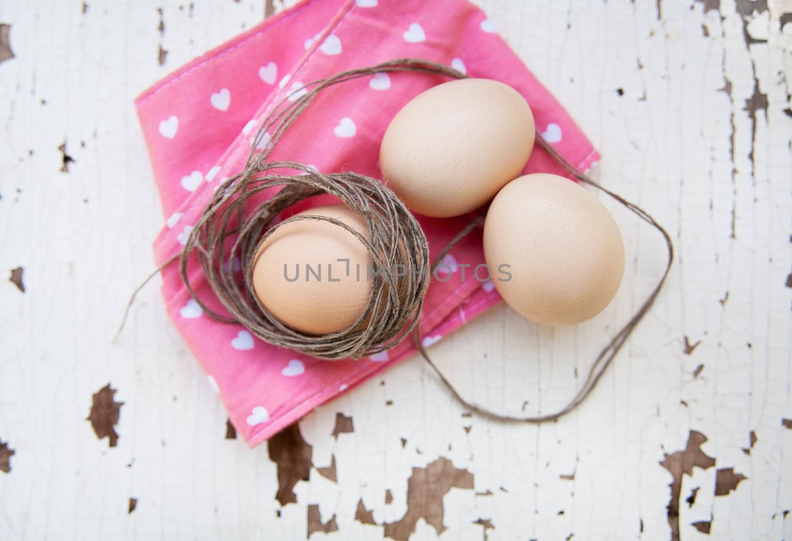 Eggs on pink tablecloth and old rope over vintage cracky white wooden background. Top view