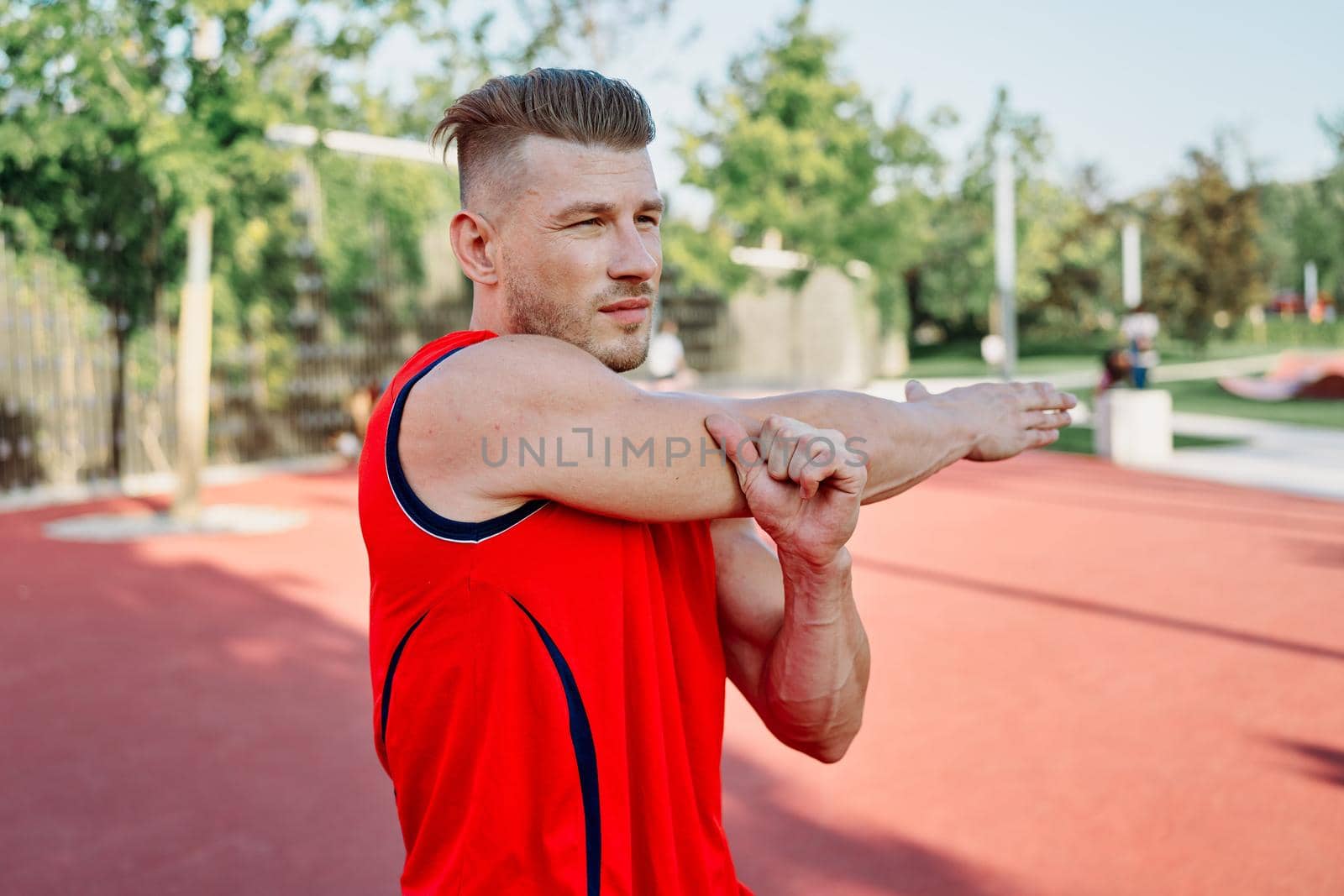 sports man in a red t-shirt on the sports ground doing exercises by Vichizh