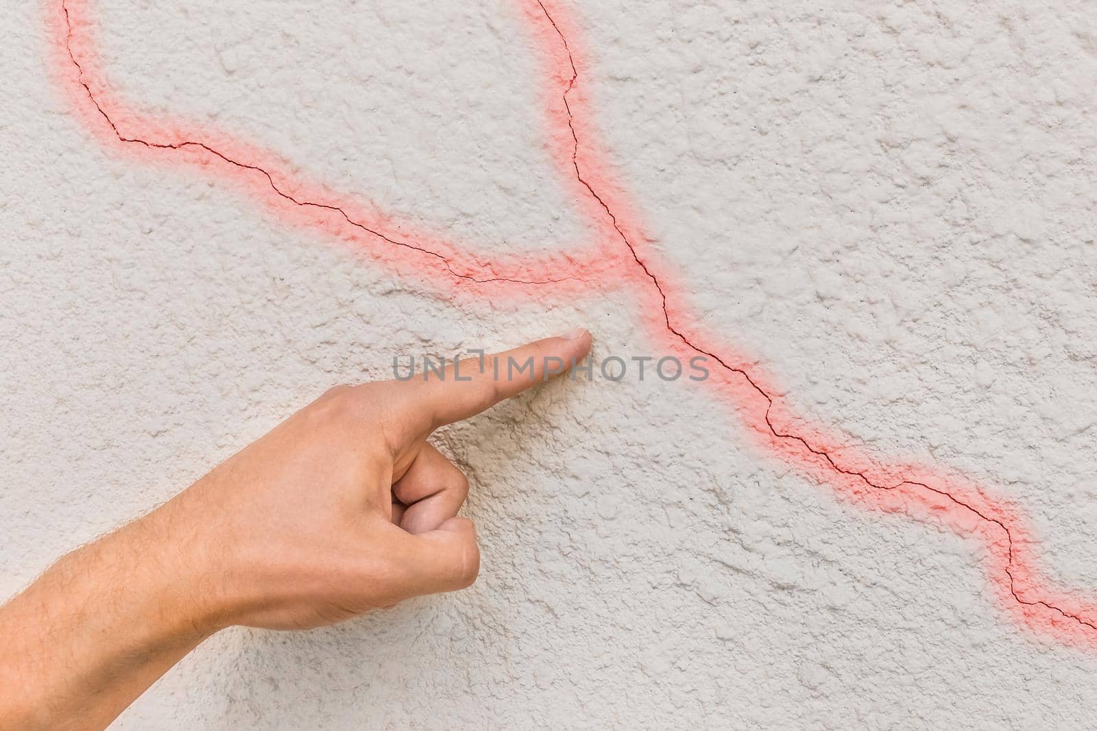 Male construction worker hand points cracks on white broken wall background. Renovation concept.