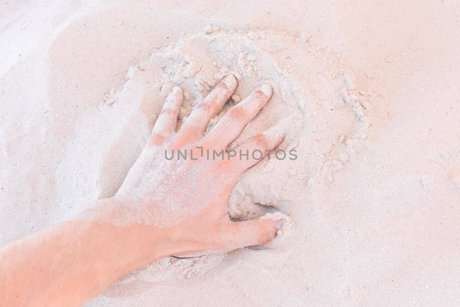 The guy's hand takes or touches the white beach sand close up.