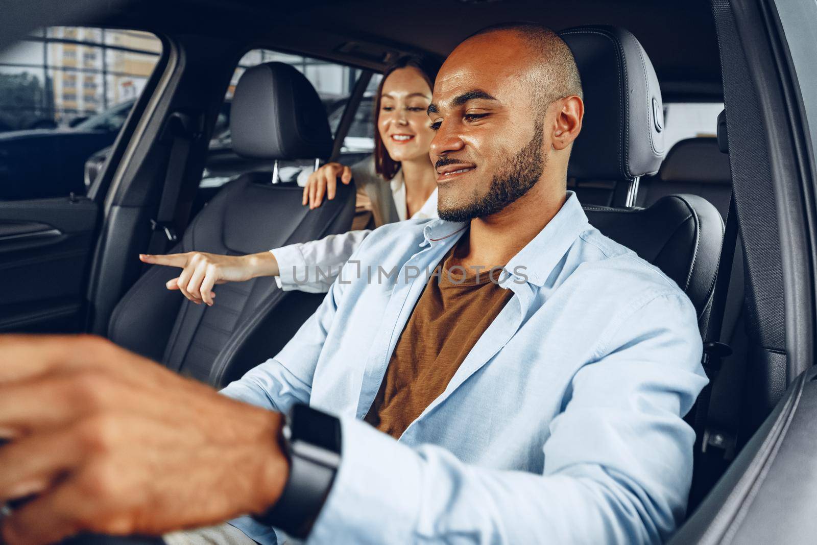 Young attractive caucasian woman salesperson in car showroom showing a car to her male African American client