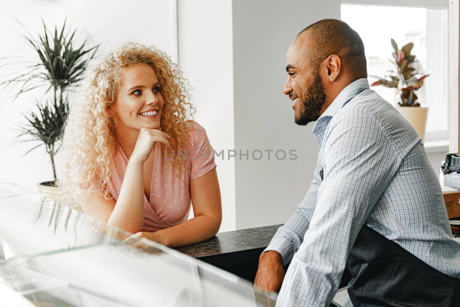 Smiling blonde woman talking to a waiter of a coffee shop at the counter table