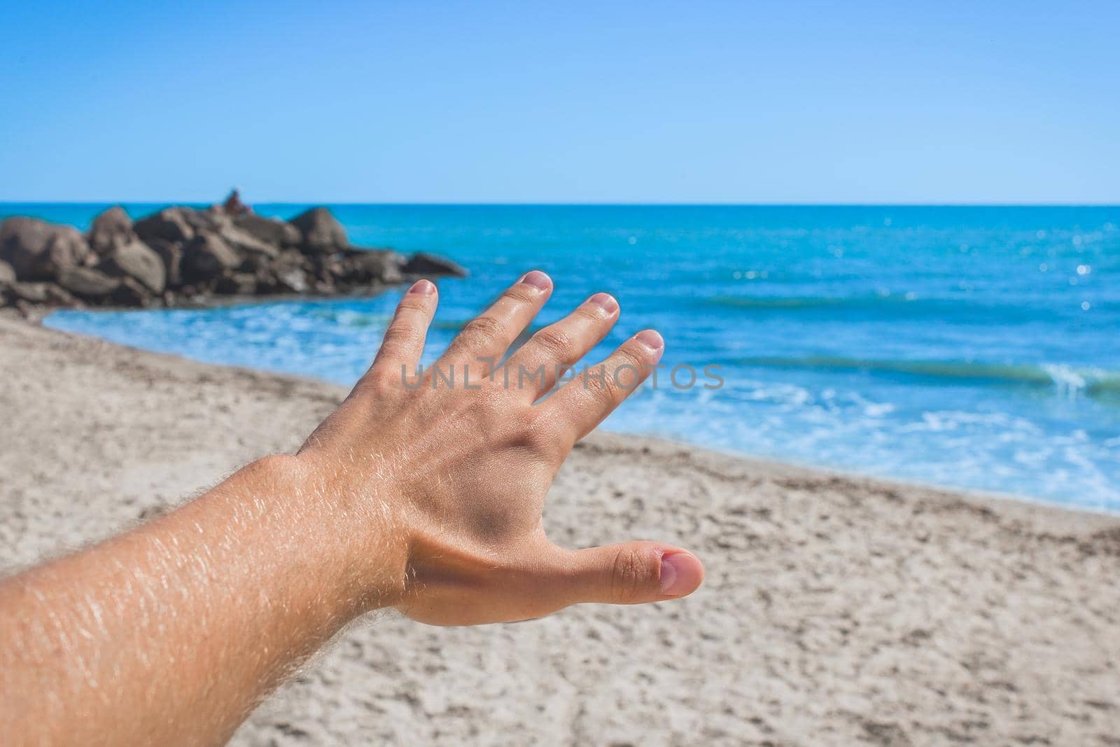 The young man stretched his hand forward to the sea and sky on the beach. The concept of freedom and rest at sea by AYDO8