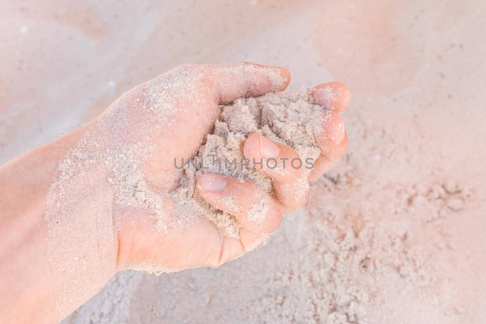 The guy's hand takes or touches the white beach sand close up.