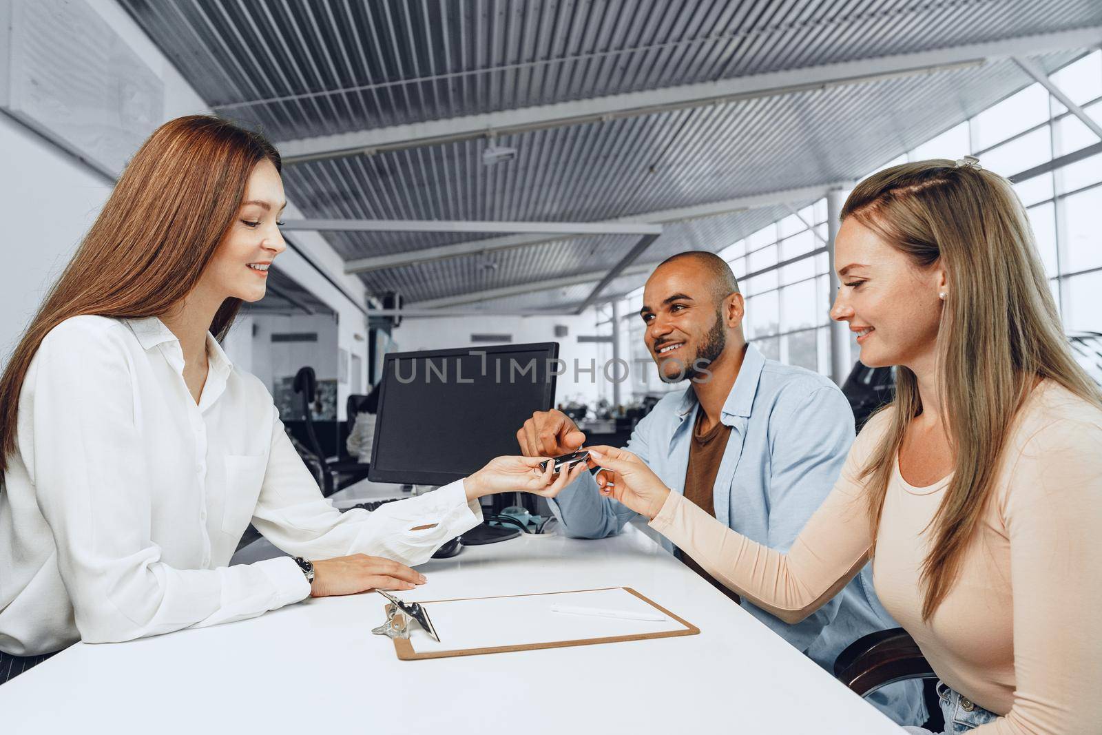 Cheerful couple taking keys of their new car in car dealership from saleswoman