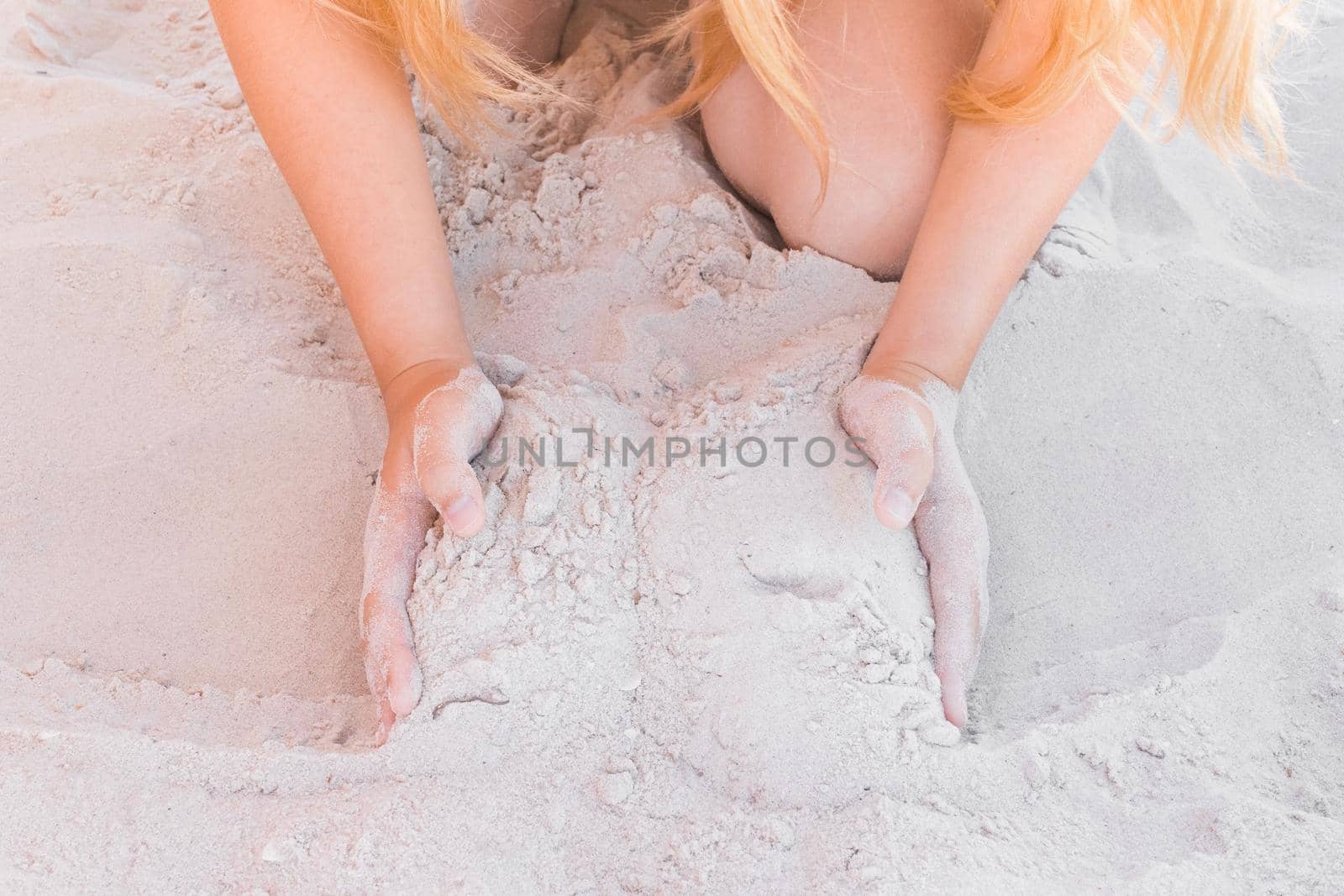 The hands of a young girl hold a pile of white sand close-up.