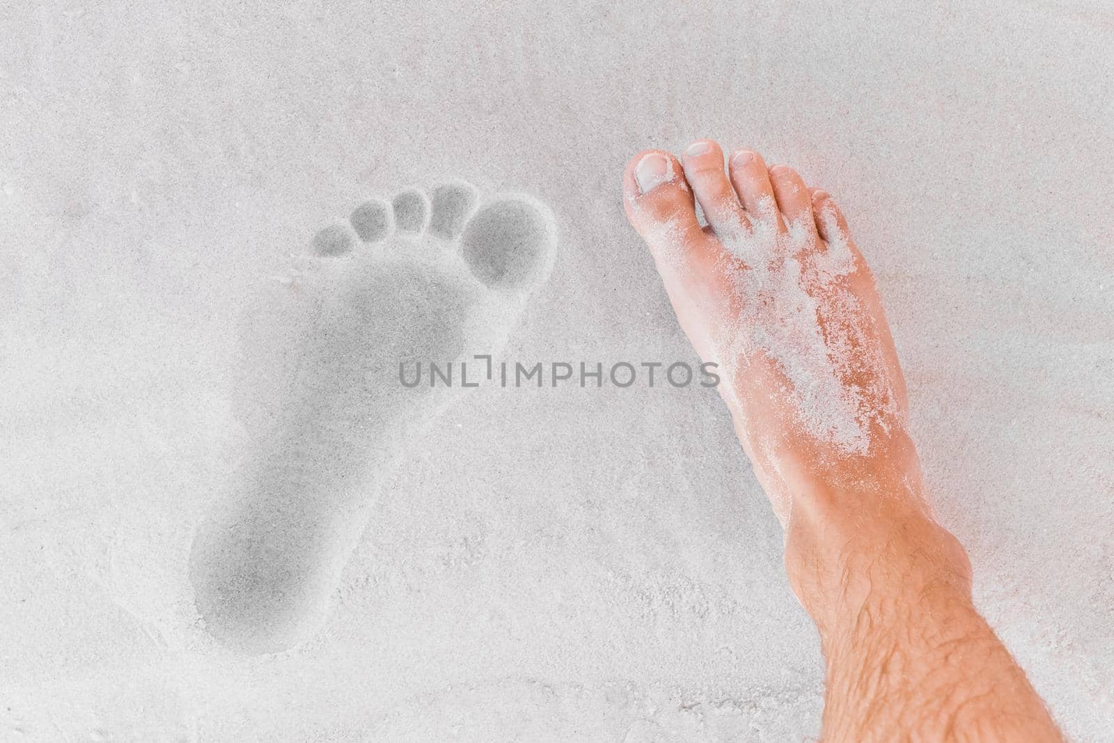 The men's leg stands next to its footprint on the beach sand close-up.