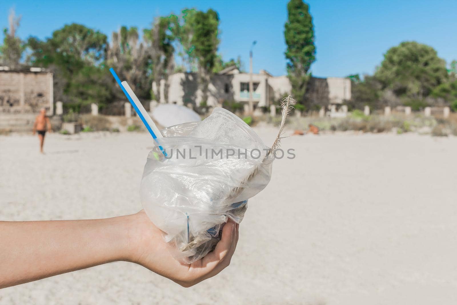 The girl's hand holds a plastic bag with garbage on the beach. The concept of pollution and ecology. Waste disposal.