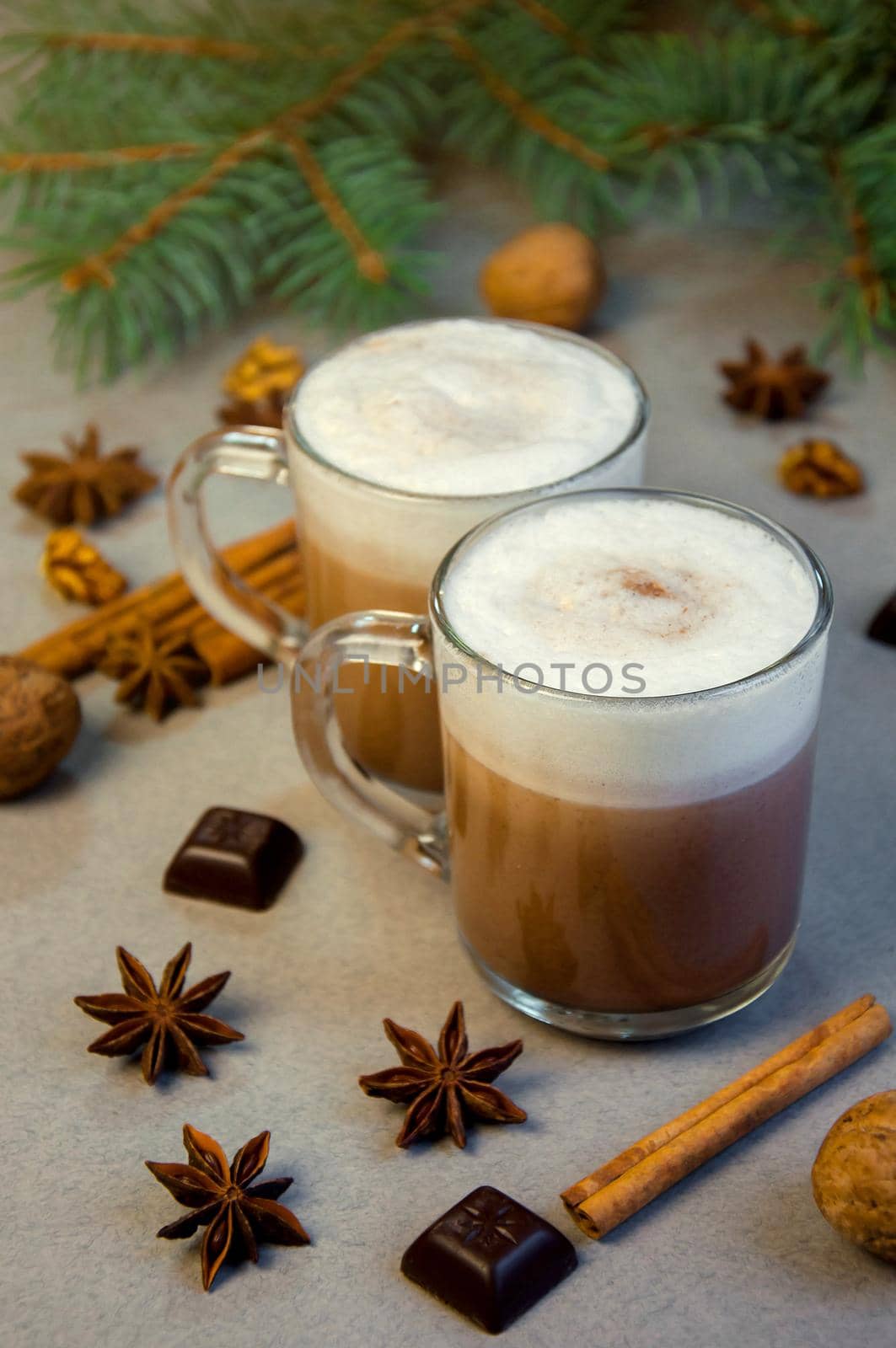 Hot Christmas Drink Cocoa Coffee or Chocolate with Milk Cream in a Small Transparent Cup. Fir Tree Branch, Nuts, Cinnamon Sticks Star Anise on a Grey Background. Winter time. New Year