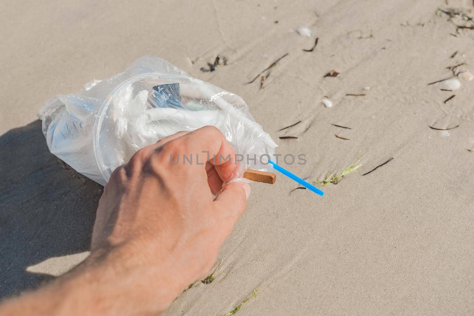 Man's hand picks up or collects garbage on a seaside beach close-up by AYDO8