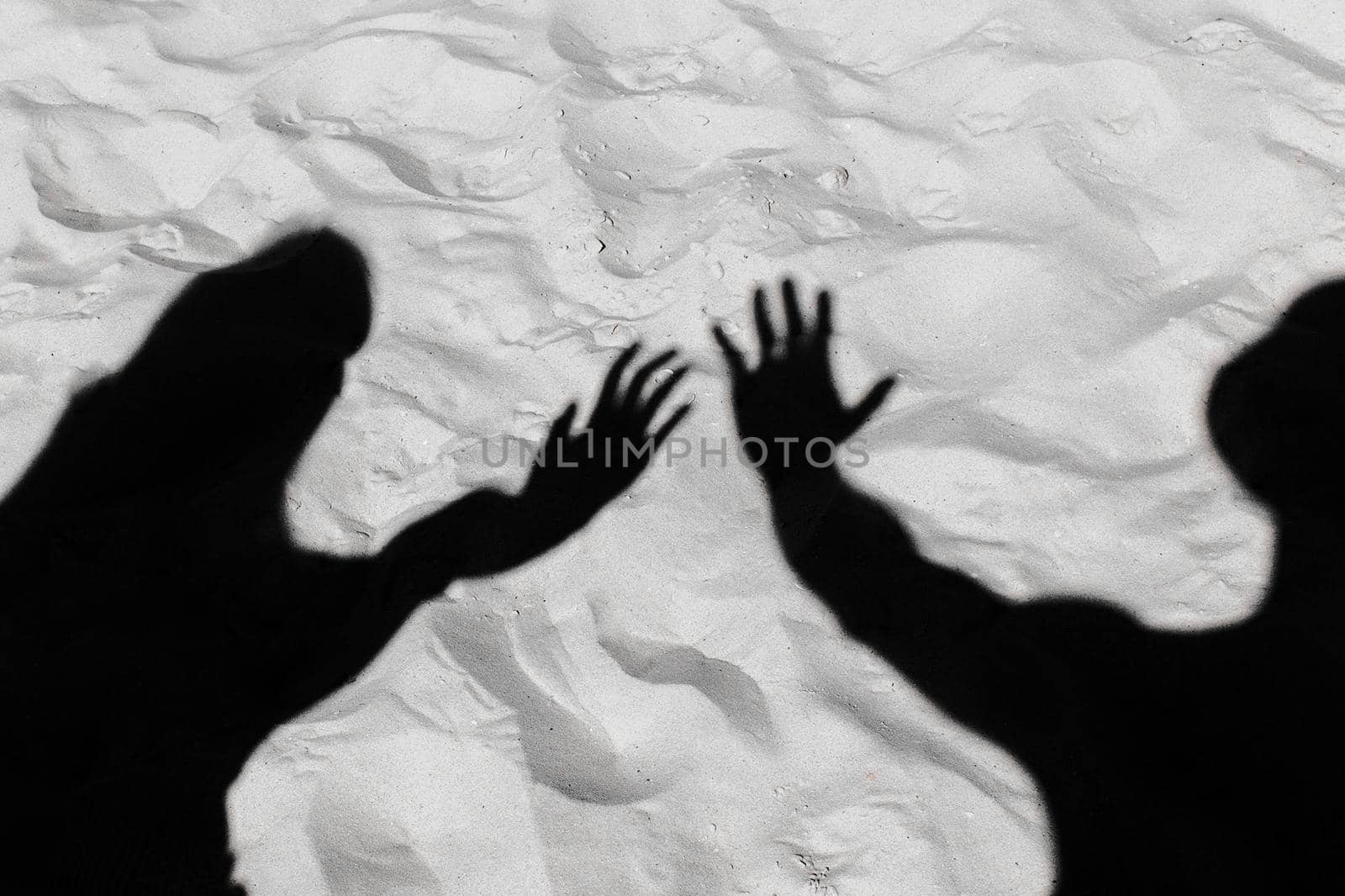 The black silhouette of a guy and a shadow girl stretched their arms forward on the white beach sand background by AYDO8