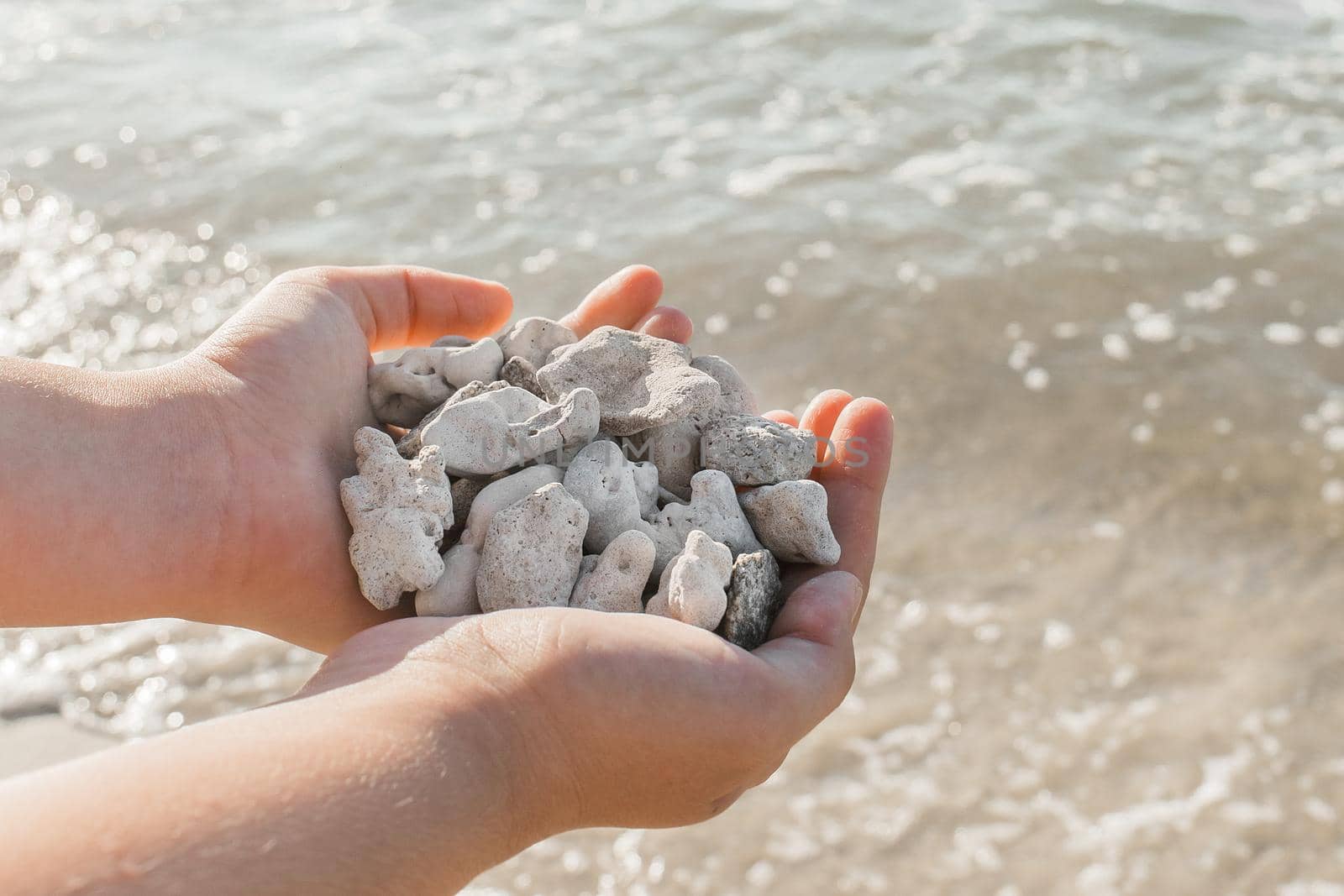 The girl's hands hold a pile of stones close up against the sea water by AYDO8