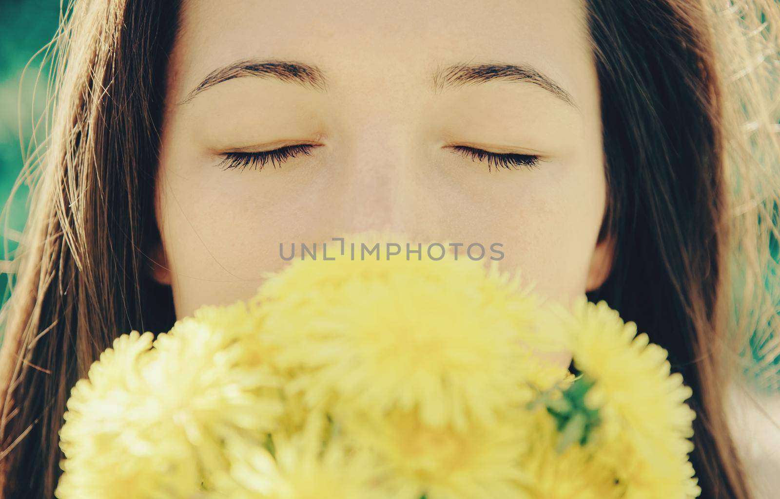 Portrait of beautiful girl with closed eyes with bouquet of yellow dandelions outdoor in summer, focus on eyes