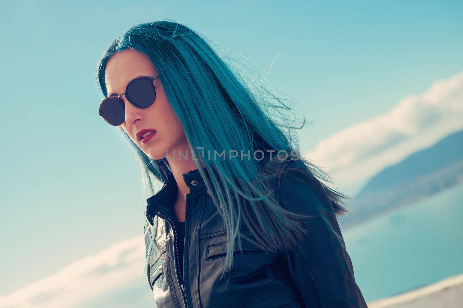 Portrait of fashionable girl wearing in leather jacket and round sunglasses with blue hair outdoor