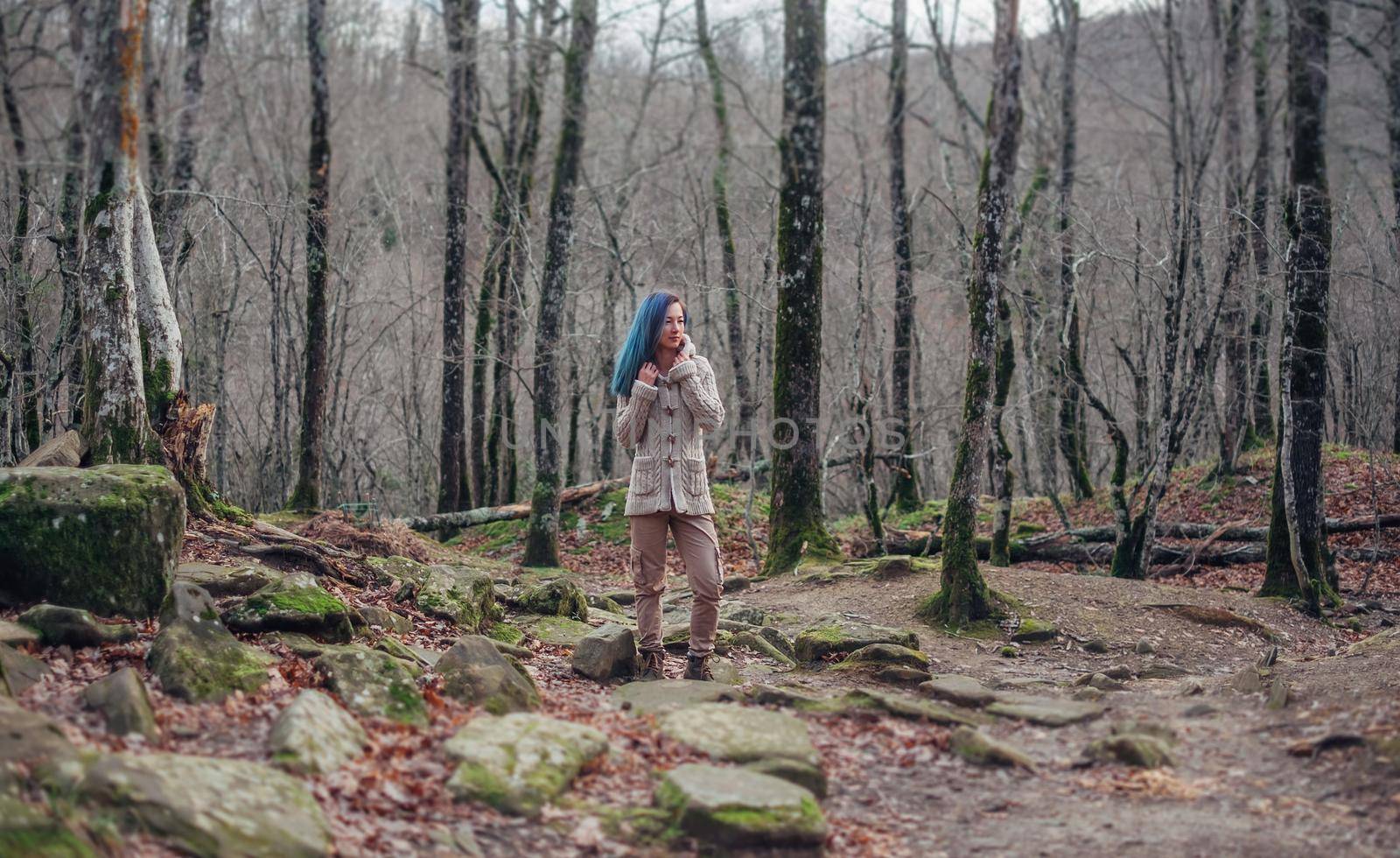 Beautiful young woman with blue hair wearing in sweater and cargo pants standing in the forest