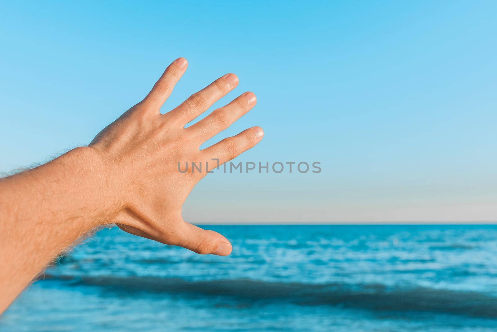 The guy's hand stretches or waves to the blue sea, the sky against the horizon line.