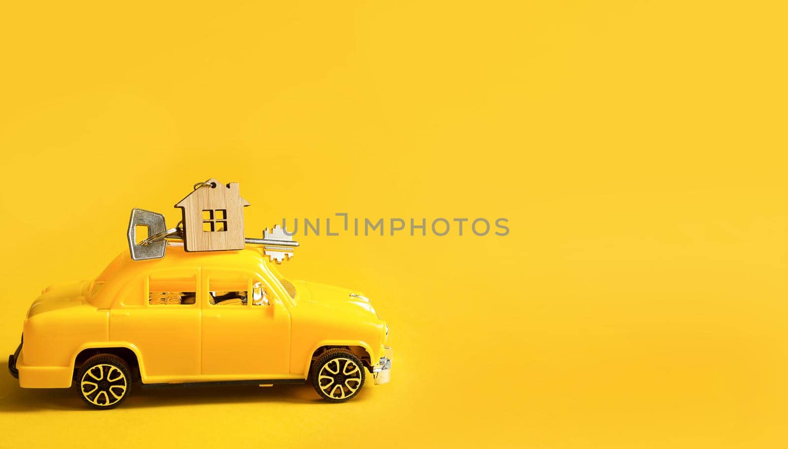 Yellow toy car with a key to the house on the roof on a color background. Moving to a new home, mortgage, buying an apartment, taxi. Copy space. by Simol