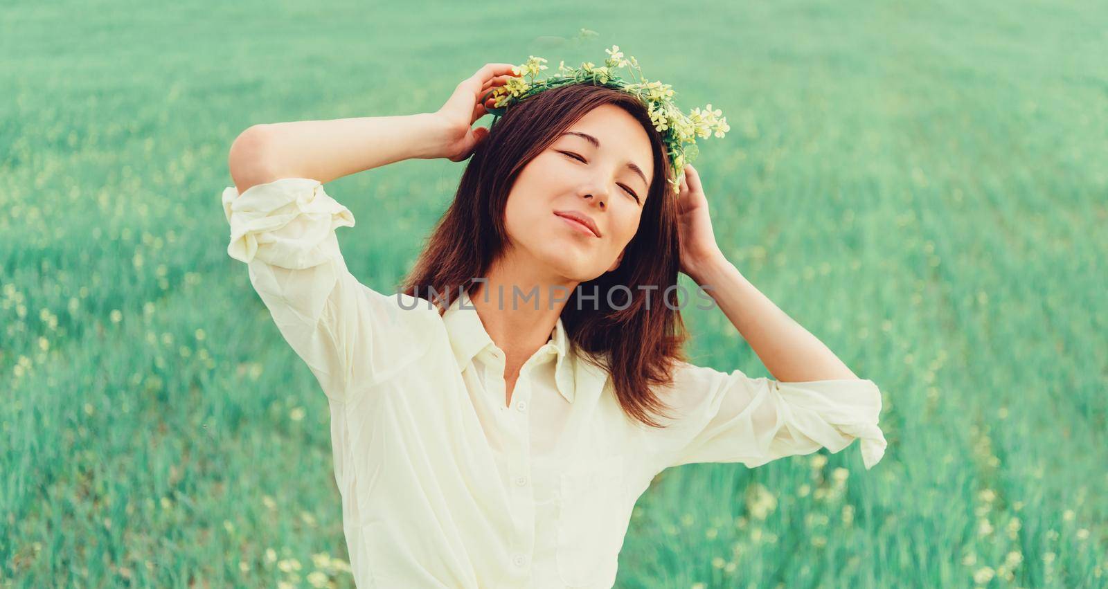 Smiling beautiful young woman with wreath of flowers enjoying a summer day on meadow