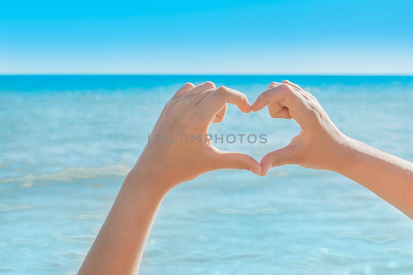 The hands of a young girl show a gesture of heart and love for the sea, rest and freedom.
