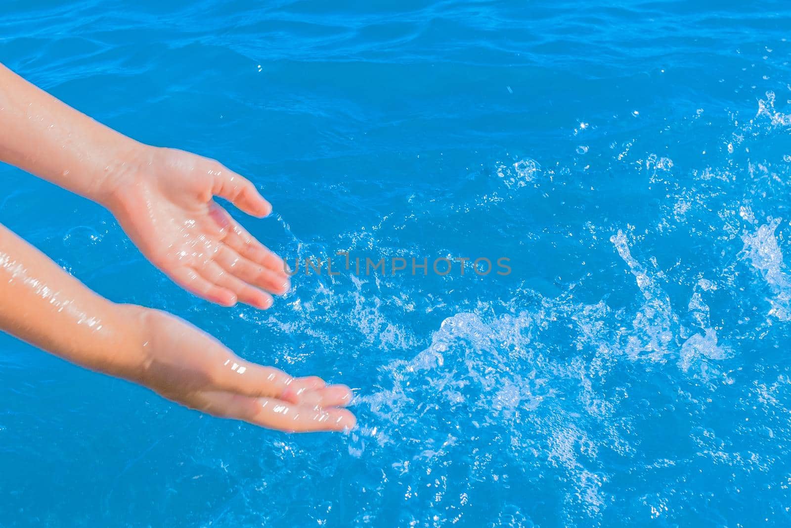 The hands of a young girl make splashes of blue pure sea water close-up by AYDO8