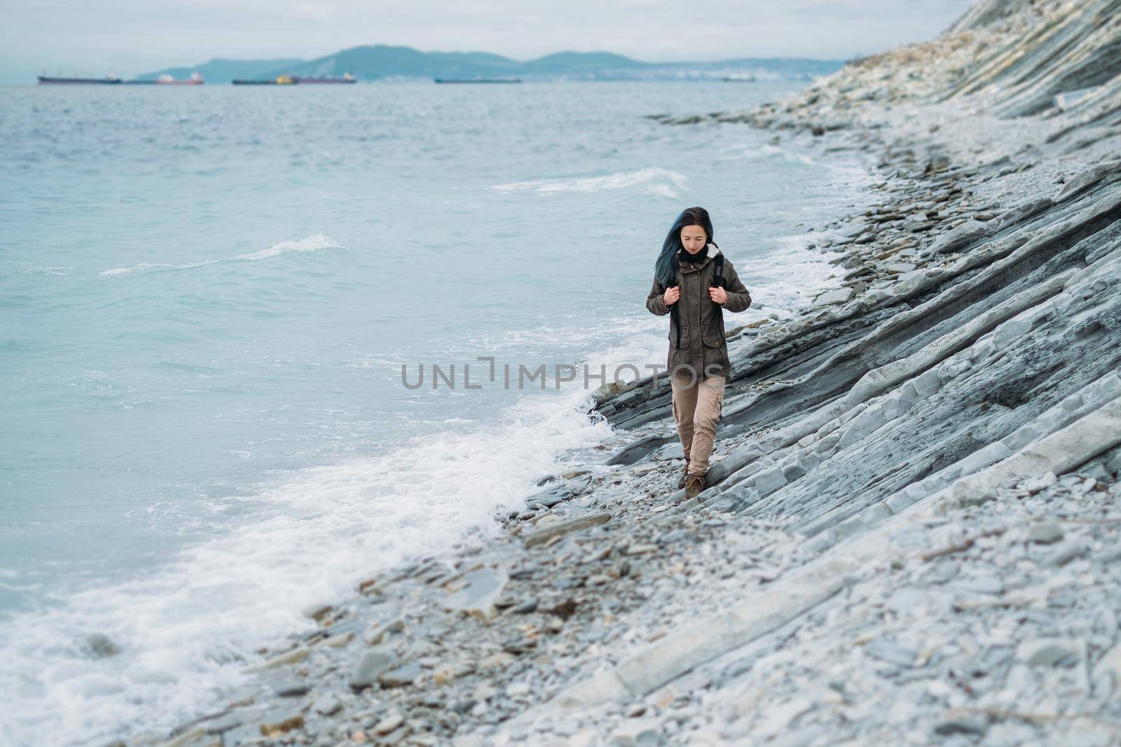 Girl wearing in warm clothing walking on coast near the sea in winter or autumn season