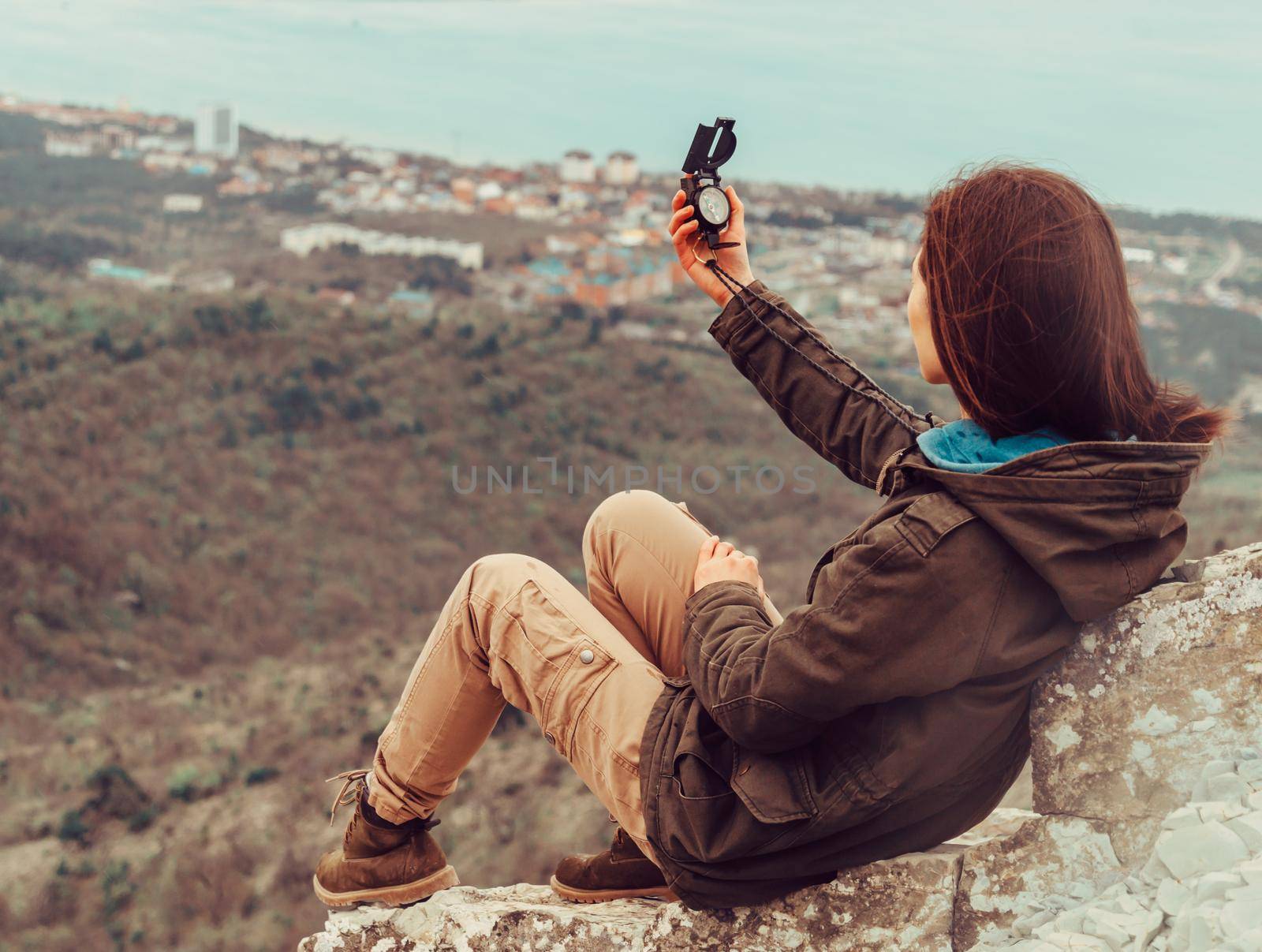 Hiker young woman sitting in the mountains and searching direction with a compass outdoor